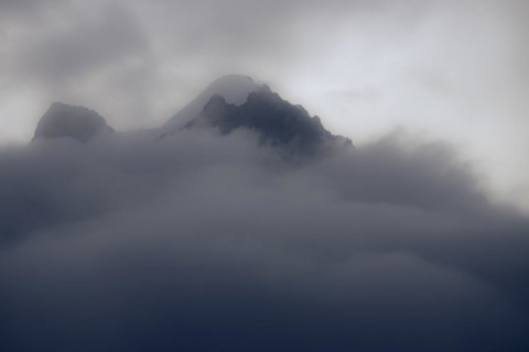 Peak of Piz Rosegg in dramatic clouds at blue hour