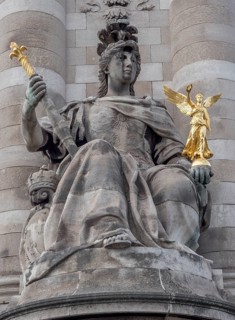 A sculpture of a woman with another small golden sculpture in her hand at the beginning of a column on the Pont Alexandre III