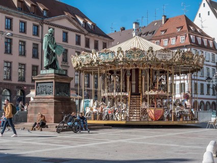 Statue de Johannes Gutenberg and next to him the children's museum carousel Merry go round Gutenberg at Place Gutenberg