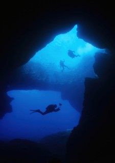 Diver underwater photographer swims dives through large underwater cave grotto Blue Dome Blue Hole on west coast of Gozo Island