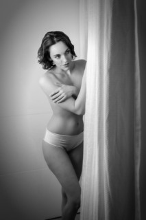 Woman dressed only in panties stands behind a curtain