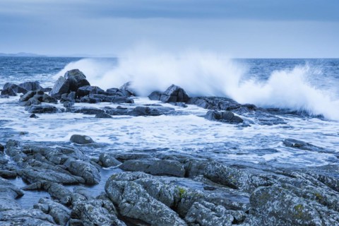 Stormy sea dashes against rocks at dawn in the blue hour