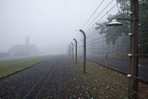 Reconstructed camp fence with crematorium in the fog at beech forest concentration camp
