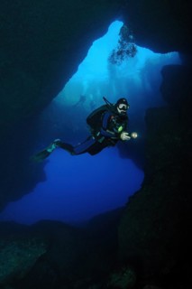 Diver with underwater lamp swims dives through large underwater cave grotto Blue Dome Blue Hole on west coast of Gozo Island