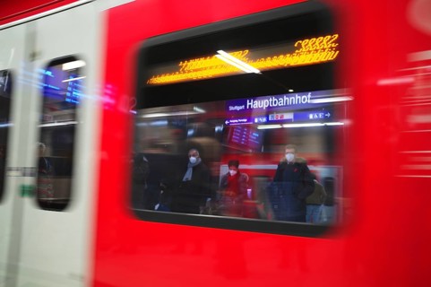 Travellers wearing Corona masks wait on the platform and are reflected in windows