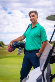 A professional golf player in a green polo shirt with the bag of clubs