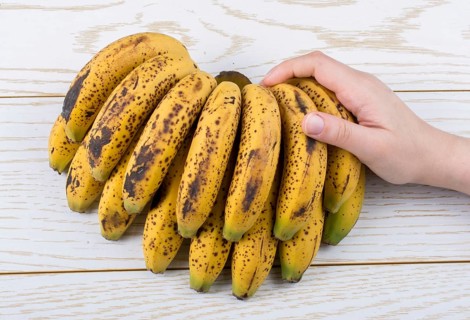 Hand holding bunch of freckled bananas on a wooden texture