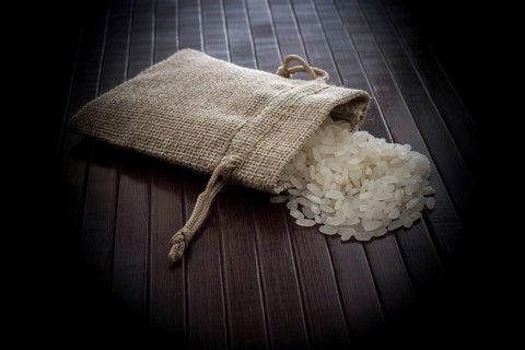 A straw pouch full of uncooked rice on a wooden background
