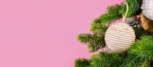 Banner with Christmas tree branches with natural ornament bauble made from beige jute rope on pink background