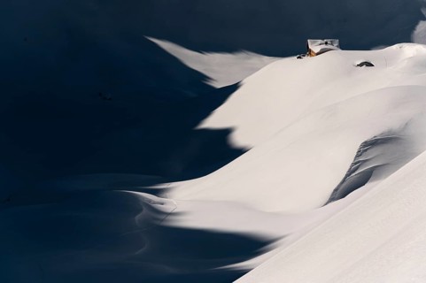 Mountain hut in deep snowy mountain landscape with light and shadow