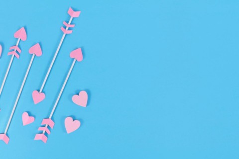 Pink cupid's arrows with heart shaped tips on blue background with copy space