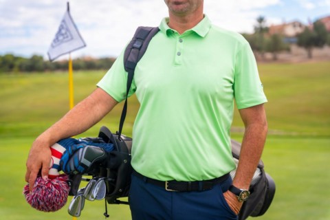 A male golfer walking down the fairway carrying bags