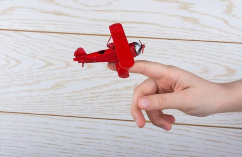 Hand holding a red toy plane on a on wooden texture