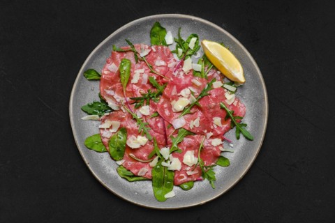 Top view of marbled beef carpaccio with arugula and chard leaves