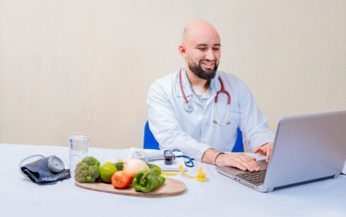 Nutritionist doctor using laptop at workplace. Bearded nutritionist doctor working on laptop at desk