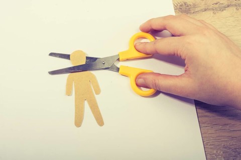 Scissors cutting paper man's head on white paper on wooden background