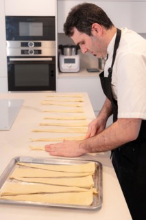A man baking croissants picking up the triangular cuts from the puff pastry