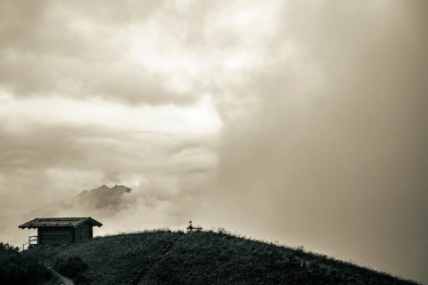 Mountain hut with bench and climber and dramatic clouds in the background