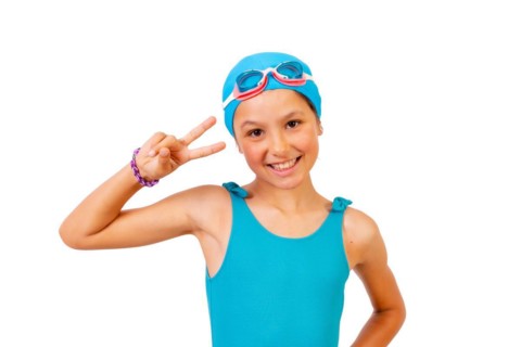 Portrait of girl with swimsuit and diving goggles for swimming lessons in the pool making the victory symbol. White background