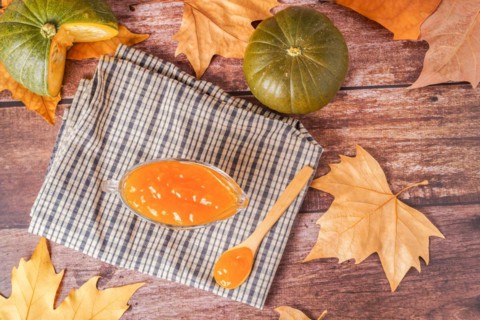 Homemade pumpkin marmalade in a glass jar with dried leaves on a white cloth on a wooden table