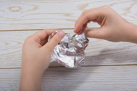 Hand tearing a heart shaped aluminium foil on a wooden background