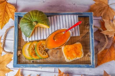 Top view of homemade pumpkin marmalade in a glass jar on a wooden tray with dried leaves