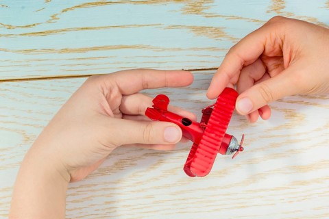 Hand holding a red toy plane on a on wooden texture