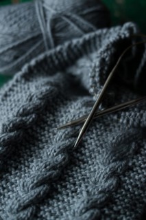 Grey knitted piece with knitting pattern and knitting needles