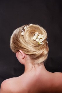 View from behind of a stylish woman with an elegant blonde hairstyle with her hair coiffed in a neat knot with a floral hair accessory and bare shoulders