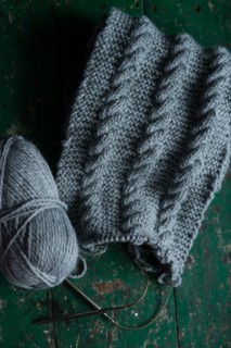 Grey knitted piece with knitting pattern and knitting needles