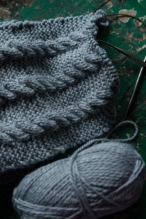 Grey knitted piece with knitting pattern and knitting needles