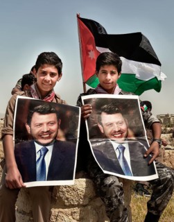Two boys in scout uniform with portraits of Jordans King Abdullah II bin al-Hussein in front of the Jordanian flag. Amman