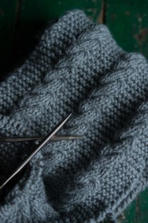 Grey knitted piece with knitting pattern and knitting needles
