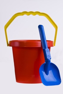 A bright red plastic childs bucket with a yellow handle and a blue spade