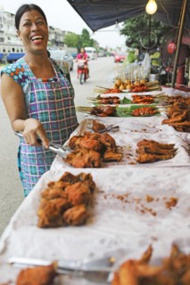 Laughing Thai woman with grilled chicken on a spit