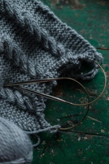 Grey knitted piece with knitting pattern and knitting needles