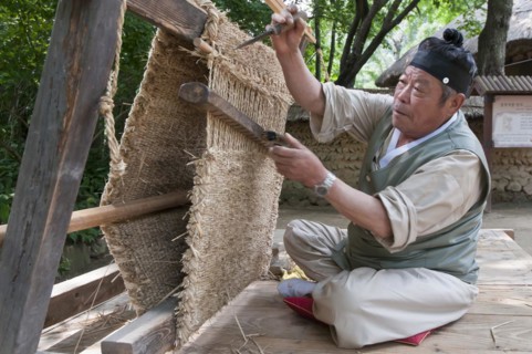 Man weaving a straw floor mat with a traditional loom