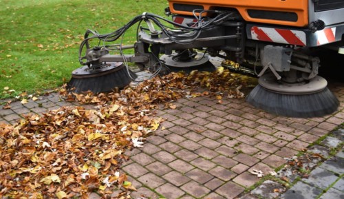 Sweeper sweeps leaves in autumn