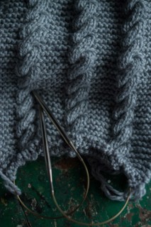 Grey knitted piece with knitting pattern and knitting needles