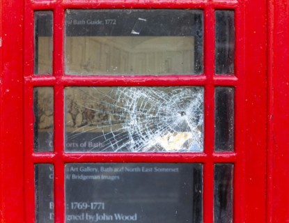 Smashed vandalised glass panel of old red telephone box