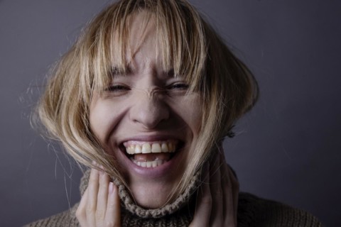 Young woman with turtleneck jumper and long hair laughs into camera
