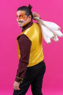 Portrait of a juggler in a waistcoat and with painted face juggling maces on a pink background