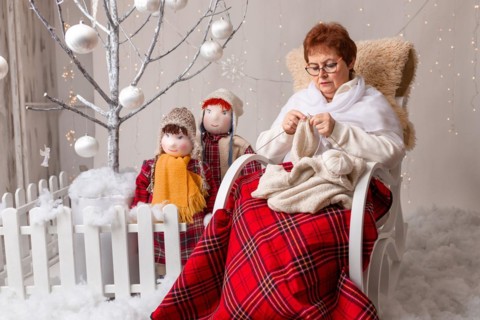 A nice elderly woman sews to knit her granddaughters in a Christmas arrangement. In studio