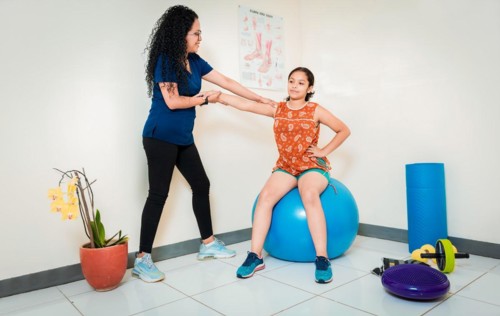 Physiotherapist assisting female patient sitting on rehabilitation ball. Rehabilitation therapy with fitness ball