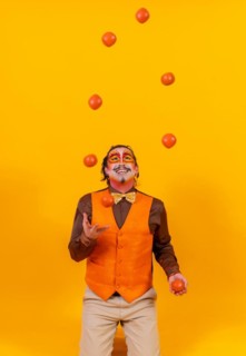 Portrait of a juggler in a vest with a painted face juggling balls on a yellow background