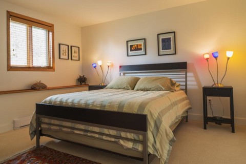 Black wood and gray metal frame queen size bed with striped beige bedspread in guest bedroom inside modern home