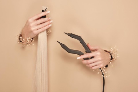 Hands with flowers hold strands of hair for extensions on a beige background. hair beauty