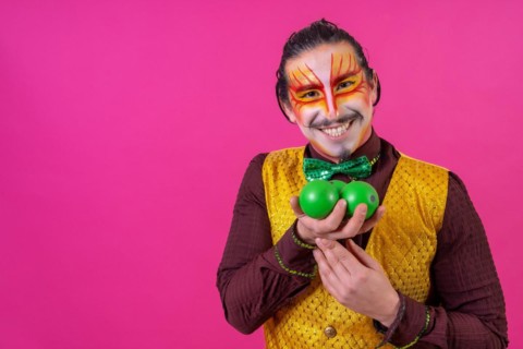 Clown with white facial makeup on a pink background