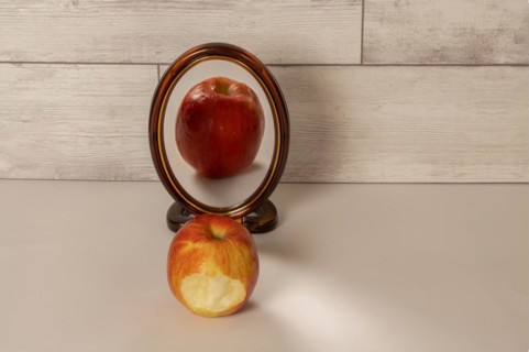 Bitten red apple reflected in a mirror isolated on a white table with copy space