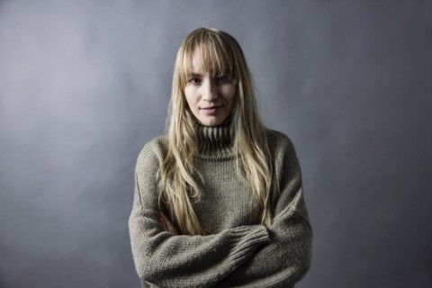 Woman with long blond hair and warm woollen jumper crosses her arms